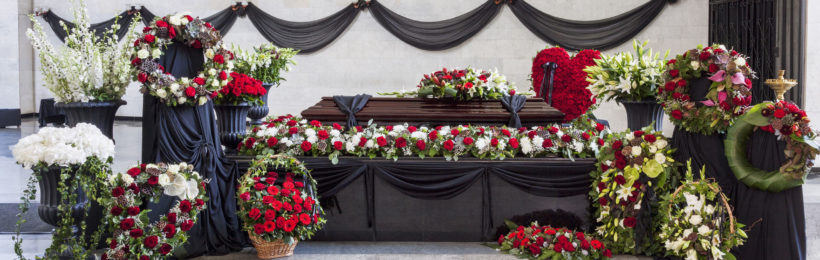 Aufgebahrter Sarg zwischen Blumengestecken auf einer Bestattung